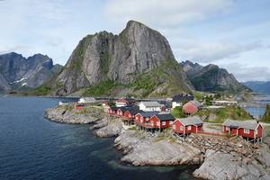 Auf den schönen Lofoten in Norwegen © Thomas Meixner auf Stelzen gebaute, rote Holzhäuser mit weißen Fensterrahmen und schwarzen Dächern auf einer felsigen Insel; im Hintergrund hohe, schroffe Felsen